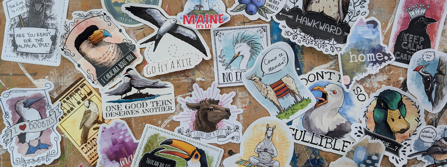 Assorted vinyl stickers featuring punny bird illustrations, llamas, alpacas, Maine themes, and humorous text arranged on a studio work surface.