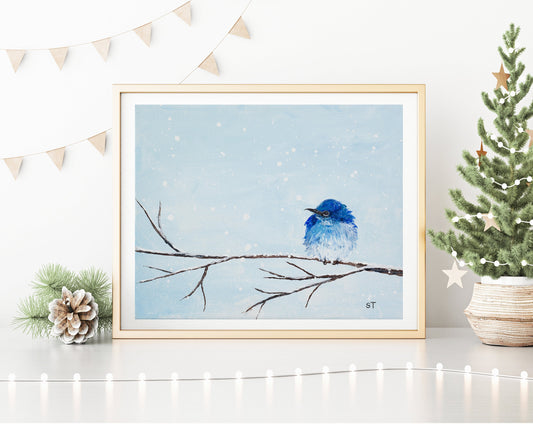 A framed print of a mountain bluebird perched on a snowy branch, displayed on a white wall with decorative string lights and a festive arrangement.