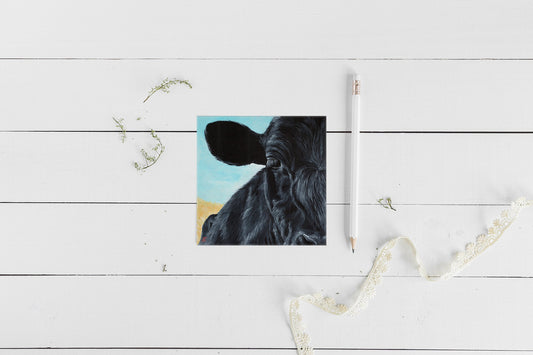 A greeting card featuring an acrylic painting of a cow's face on a white background, accompanied by an envelope and a small amount of lace for decoration.