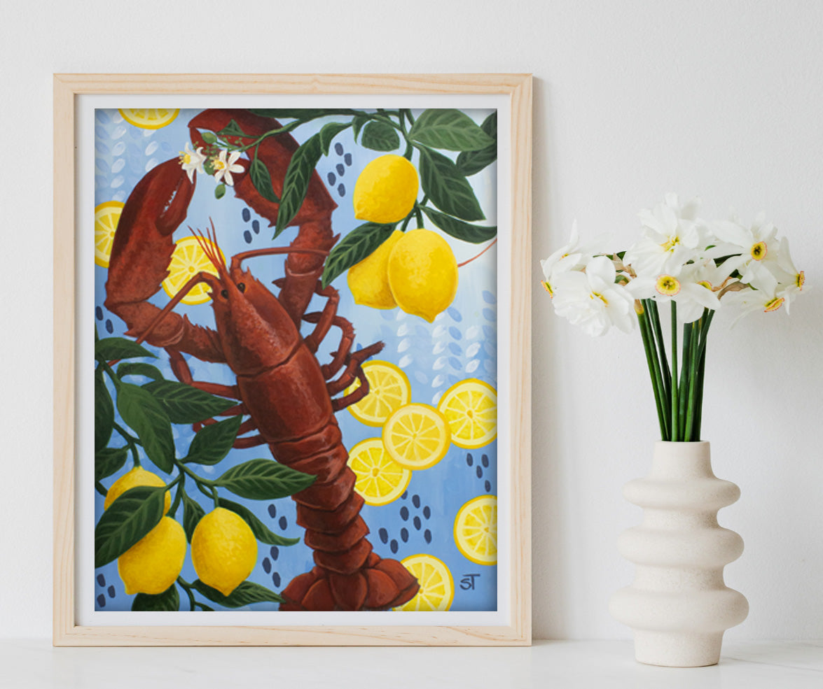 Framed artwork of a lobster and lemons on a blue background, next to a vase with flowers.