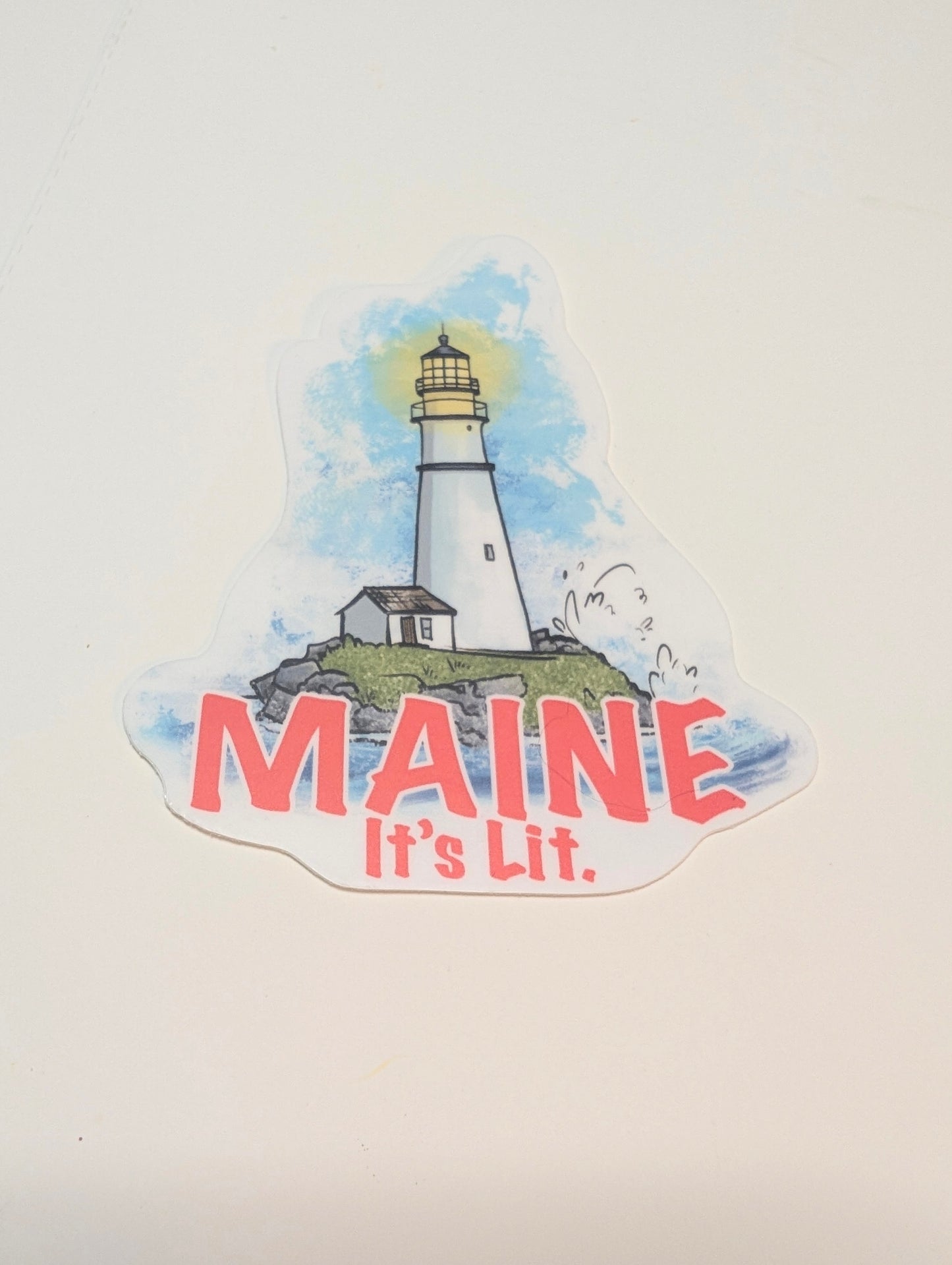 “Maine it’s lit” lighthouse vinyl sticker shown in a flat lay on a white background.