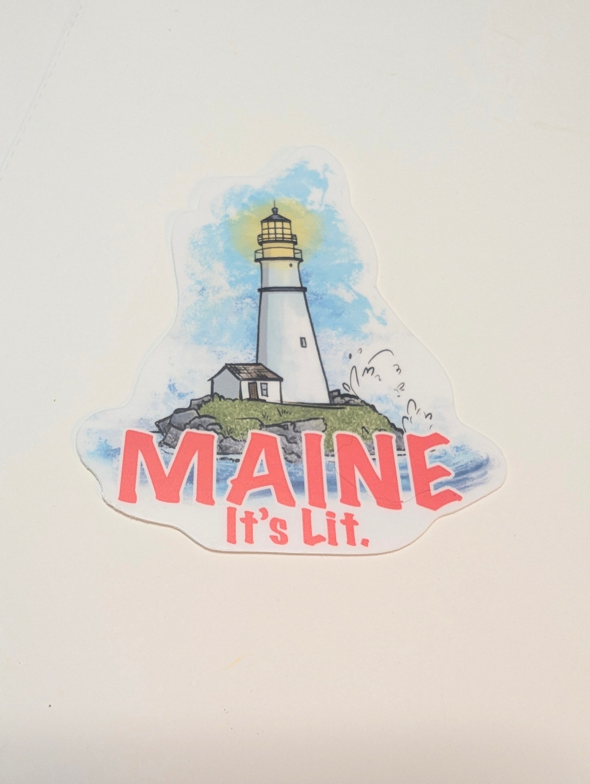 “Maine it’s lit” lighthouse vinyl sticker shown in a flat lay on a white background.
