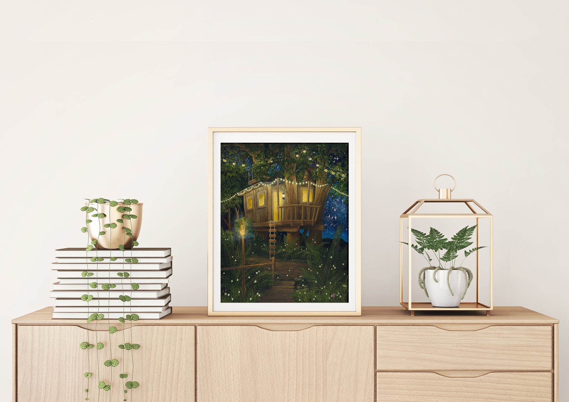 A framed art print of a treehouse featuring a starry sky and fireflies, displayed on a wooden cabinet with plants and decorative items.