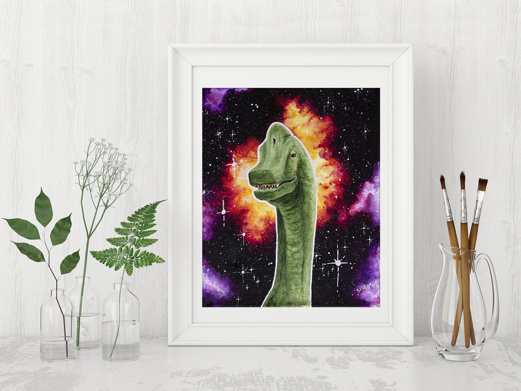 Framed art print featuring a brachiosaurus dinosaur with a space background, displayed on a white shelf with jars of greenery and paintbrushes as decor. 