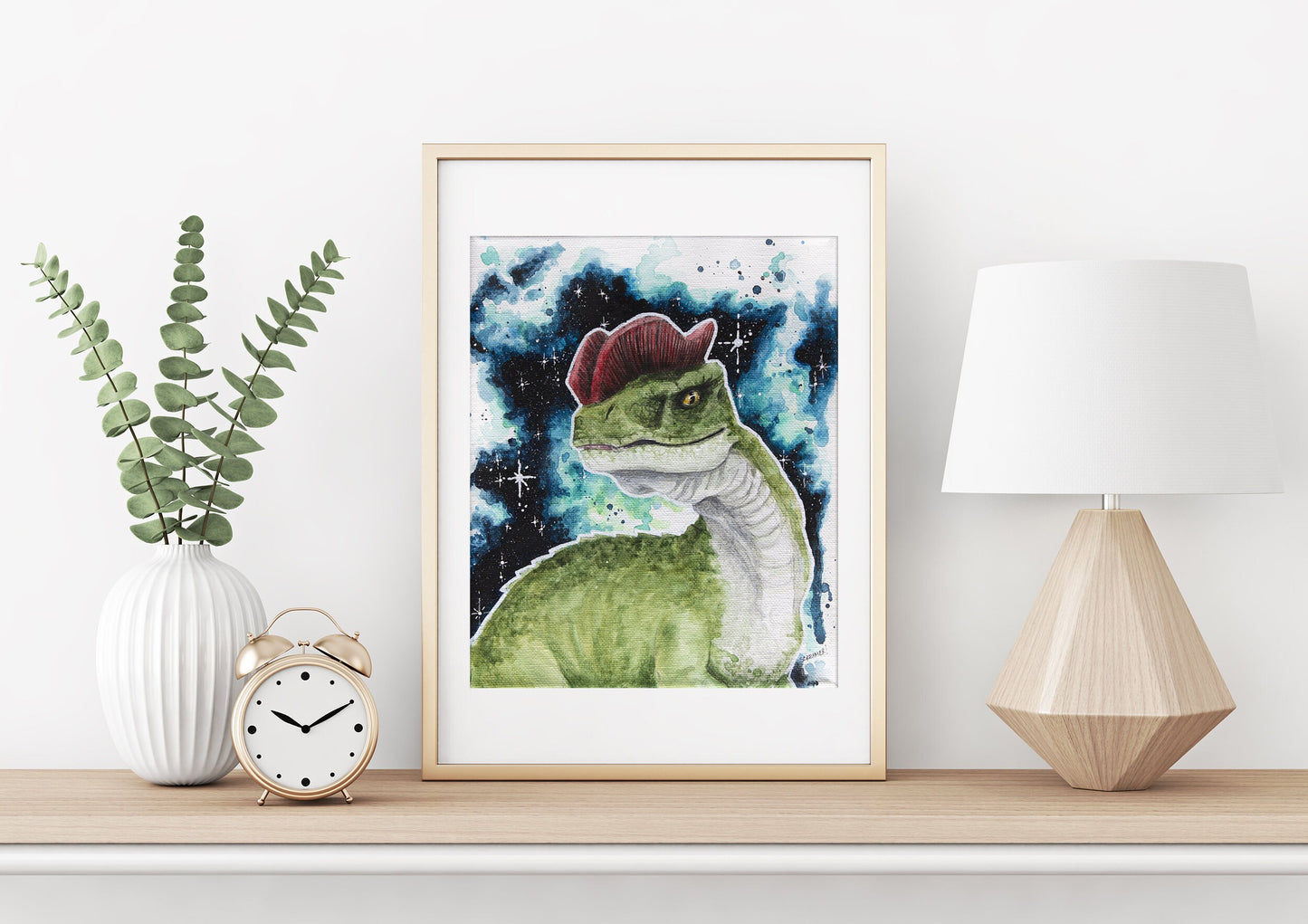 Framed Dinosaur in Space art print featuring a Dilophosaurus, displayed on a shelf with a lamp, clock, and vase of eucalyptus as decor. 