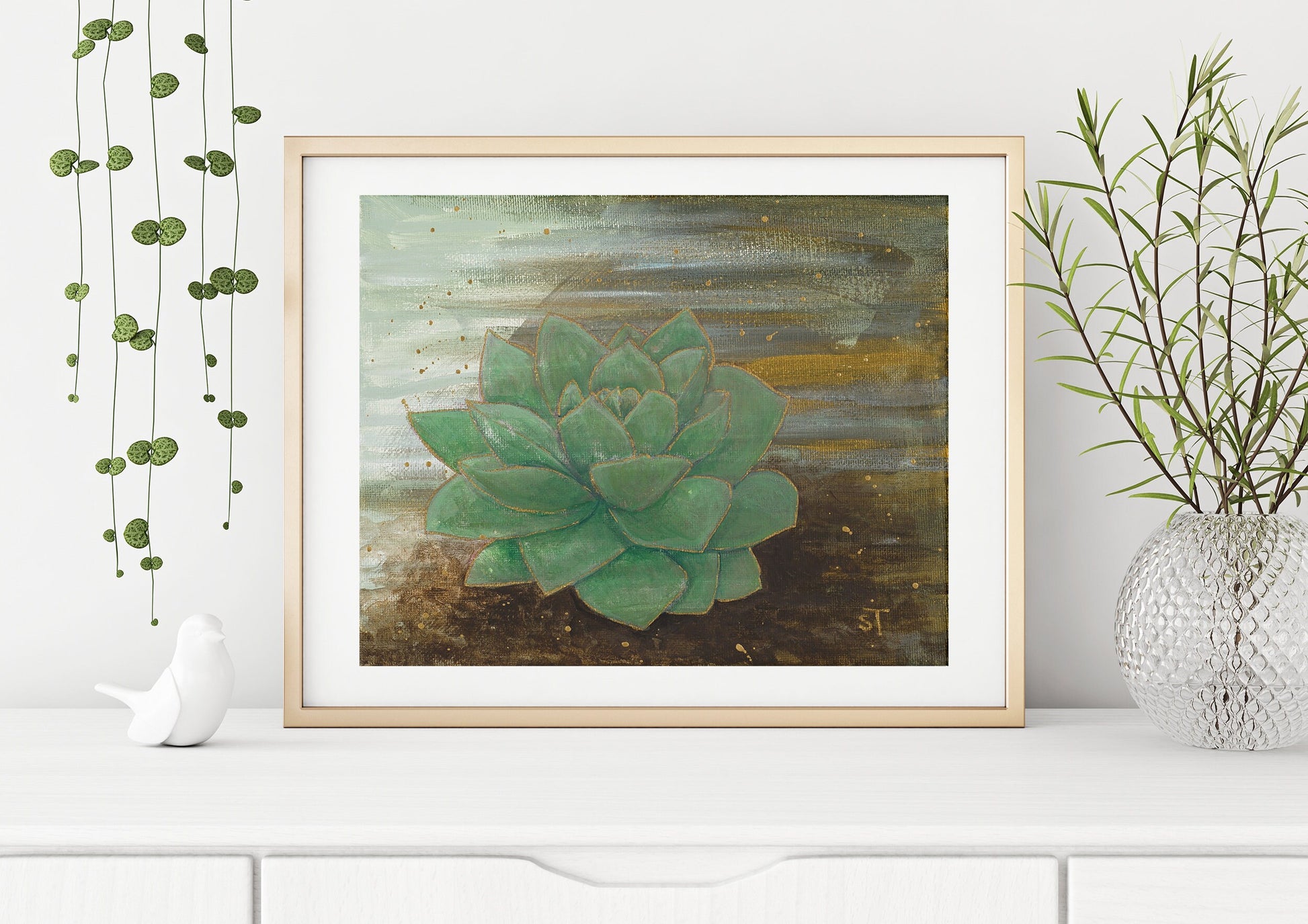 Framed green succulent art print by Sarah Terrell styled on a white shelf with hanging vines and decorative vase.